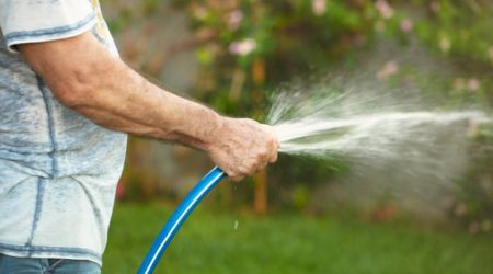 Man holding a hose to water his lawn